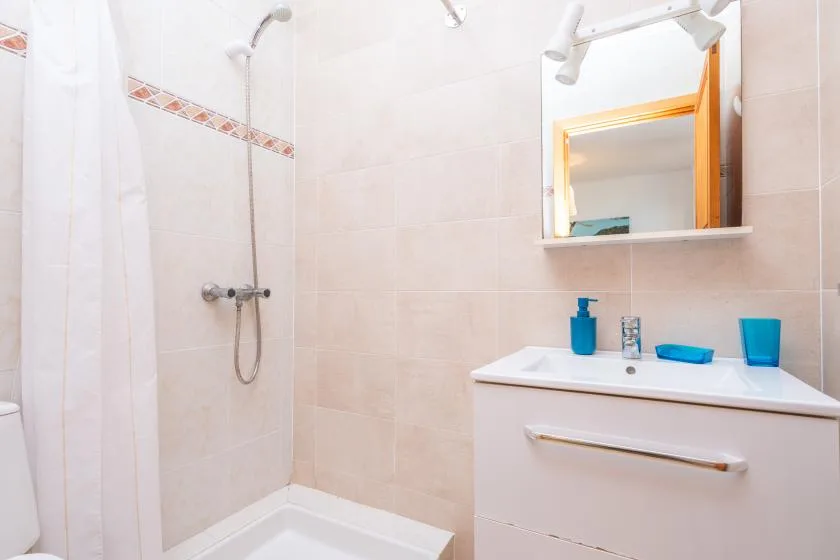 Un baño alicatado con ducha, lavabo y espejo de pared.