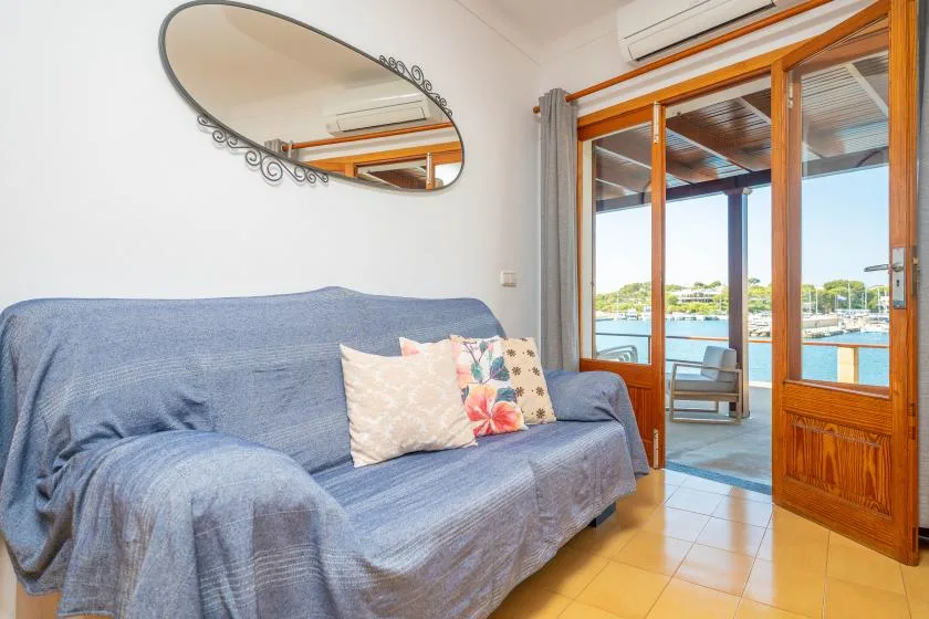 Una sala de estar con asientos azules junto a puertas de vidrio con marco de madera y vistas al agua.