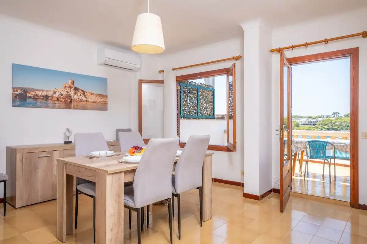 Comedor con mesa de madera y sillas junto a ventanas que dan a un balcón.