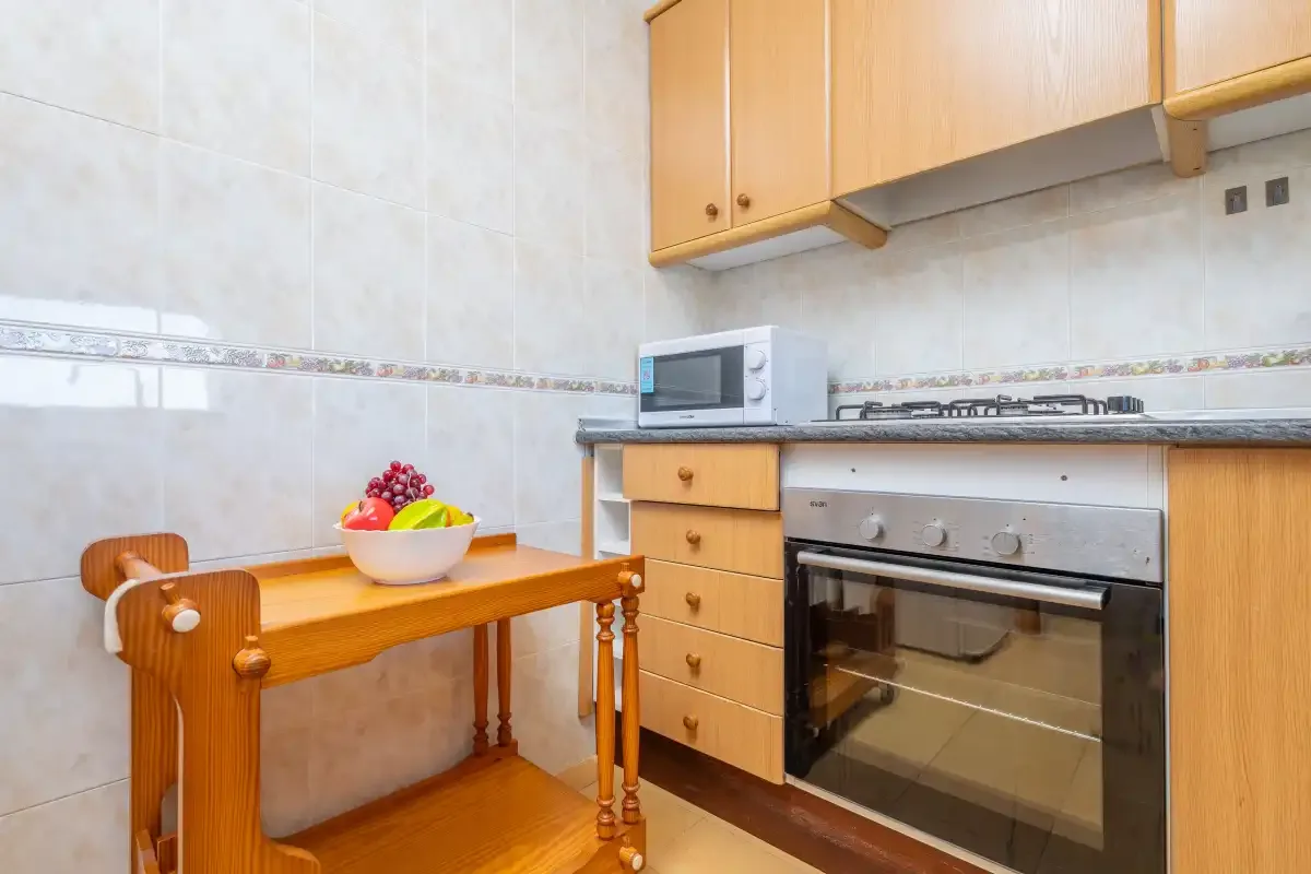 Una cocina alicatada con armarios de madera, un horno de encimera y una pequeña mesa de comedor.