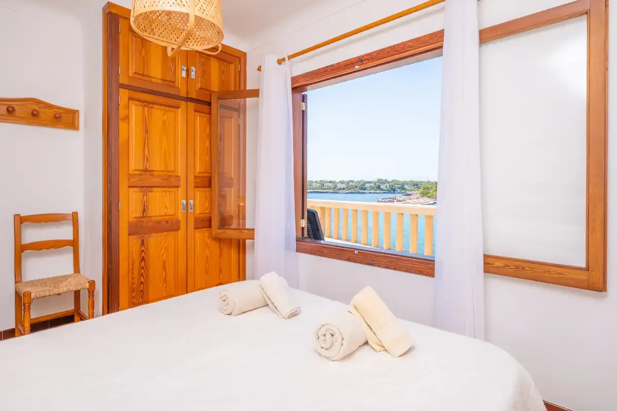 Un dormitorio con una cama junto a una ventana abierta con vistas al agua.
