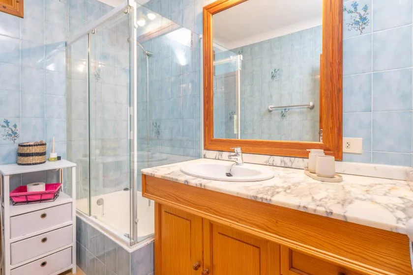 Baño con azulejos, ducha de vidrio y mueble de lavabo de madera.