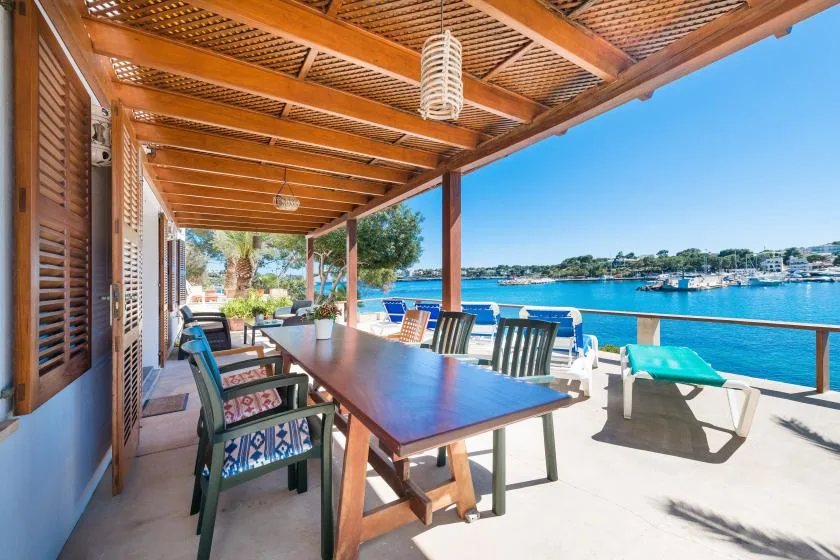 Una zona de comedor cubierta junto al agua, con una mesa larga y vistas al mar.