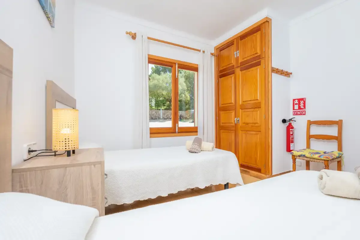 Un dormitorio luminoso con dos camas, un armario de madera y una ventana.