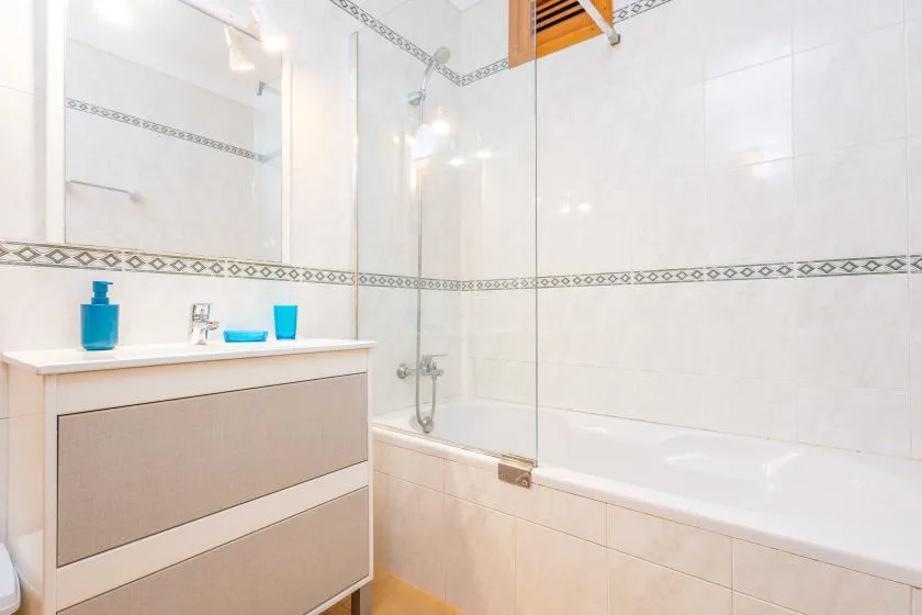 Un baño luminoso con bañera, mampara de vidrio y lavabo.
