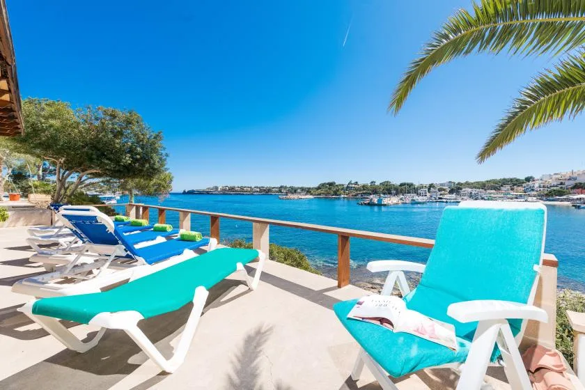 Un patio junto al agua con asientos turquesa y vistas a una bahía tranquila.