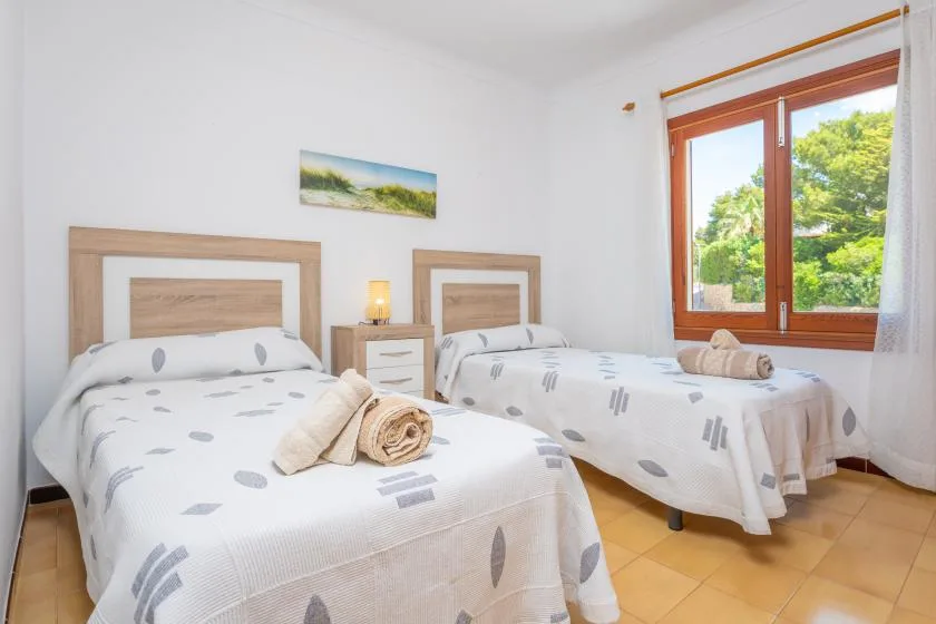 Un dormitorio luminoso con dos camas junto a una ventana amplia con vistas a la vegetación.