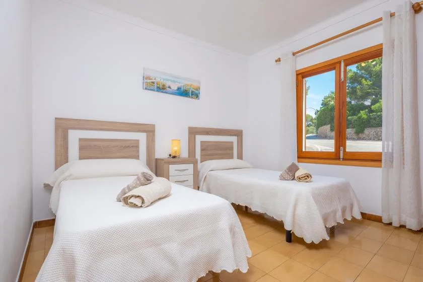 Un dormitorio luminoso con dos camas y una ventana grande con vistas a la vegetación.
