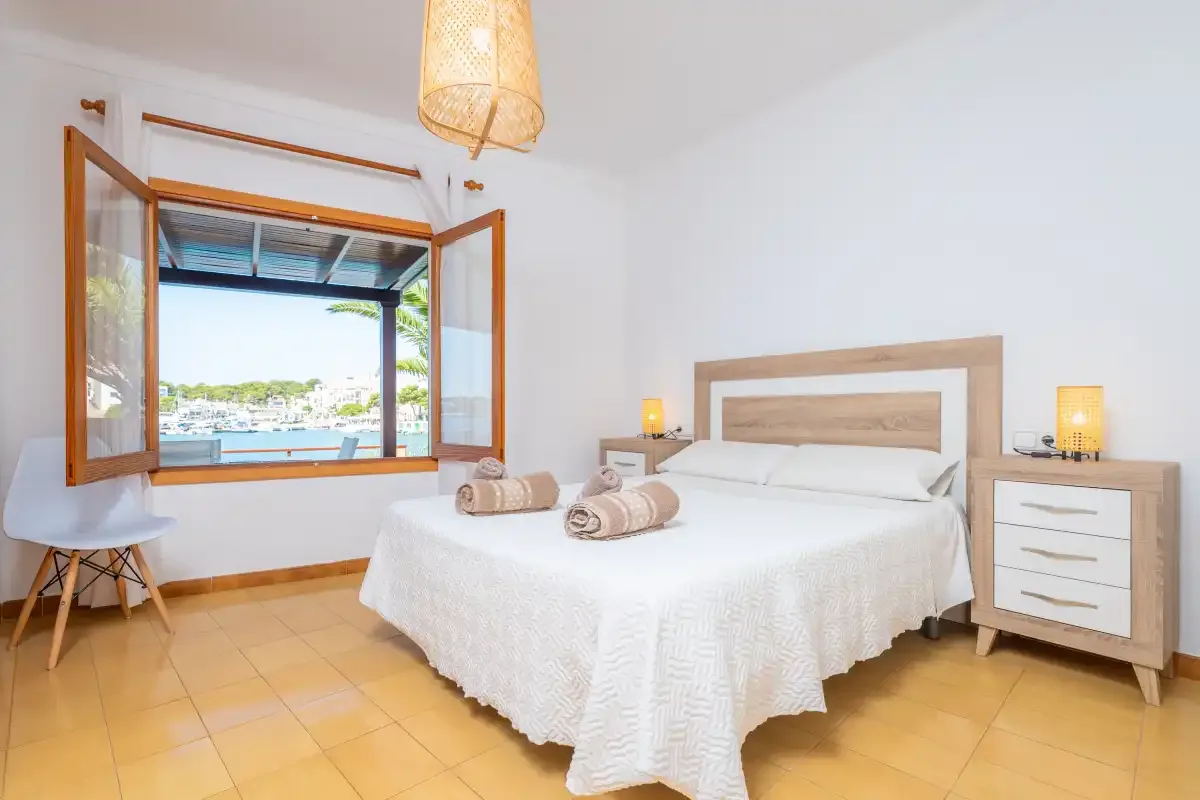 Un dormitorio luminoso con una cama y una ventana abierta con vistas al agua.