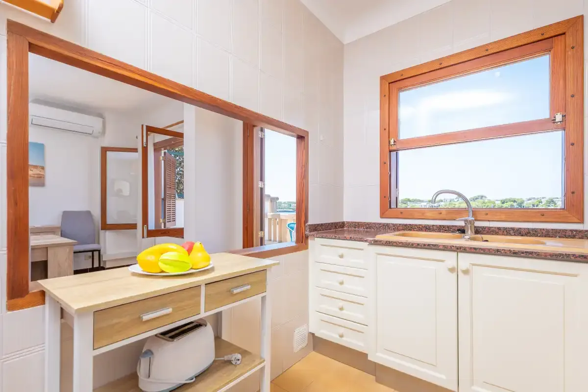 Una cocina luminosa con armarios blancos y una amplia ventana con marco de madera.