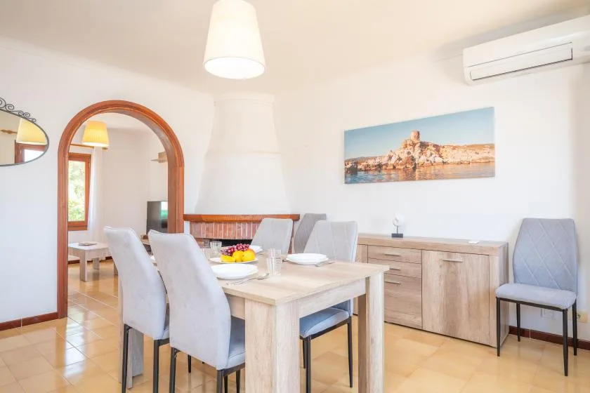 Comedor con mesa de madera clara, asientos tapizados y un aparador de madera.