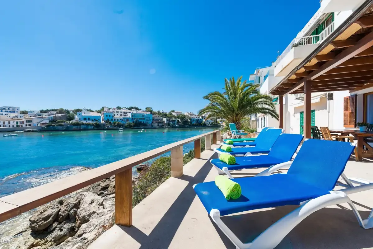Una terraza frente al mar con asientos azules mira hacia una bahía soleada.