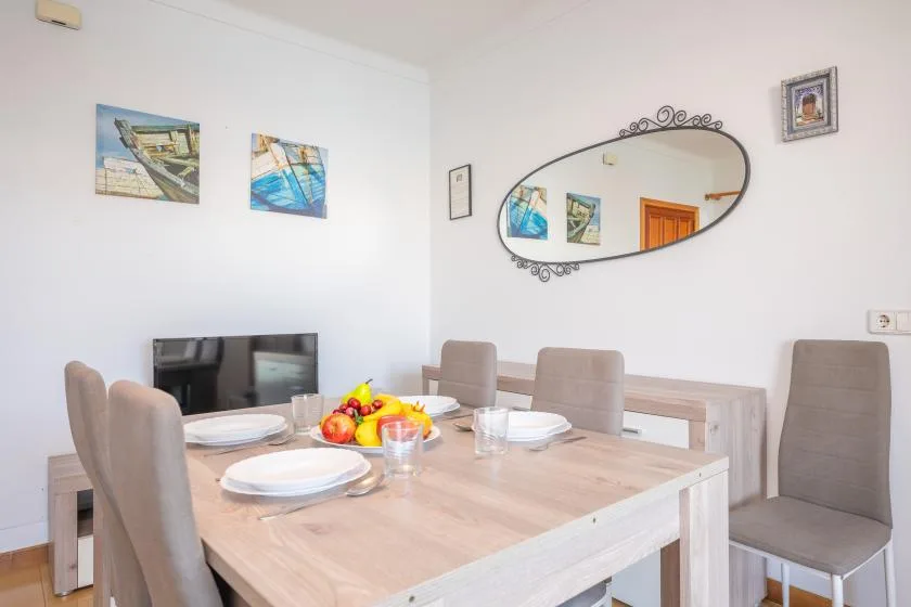 Comedor con la mesa puesta, asientos tapizados y cuadros en las paredes.