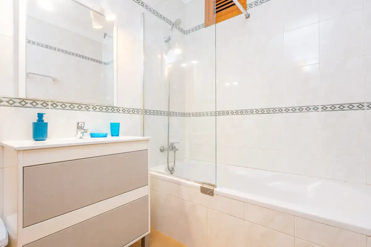Un baño luminoso con azulejos, bañera y lavabo.