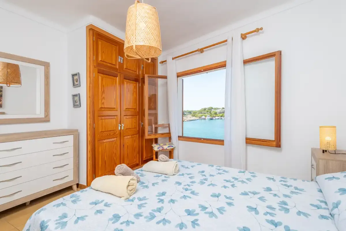 Un dormitorio con una colcha de flores azules y una ventana con vistas al agua.