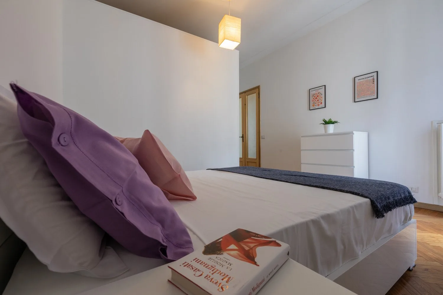 Un dormitorio con una cama, cojines de colores y una cómoda junto a la pared.