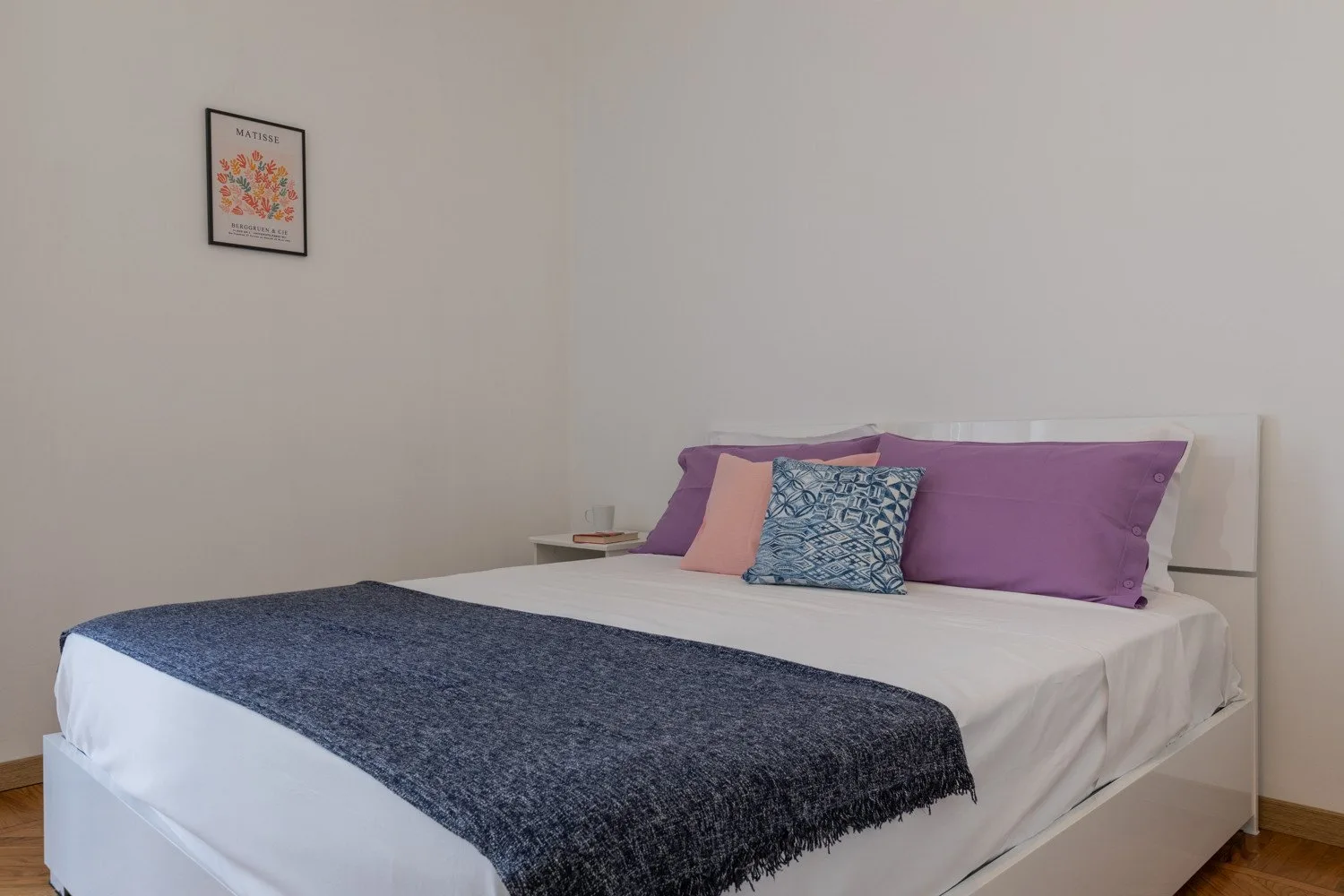 Un dormitorio con una cama bien tendida, almohadas coloridas y una manta oscura.