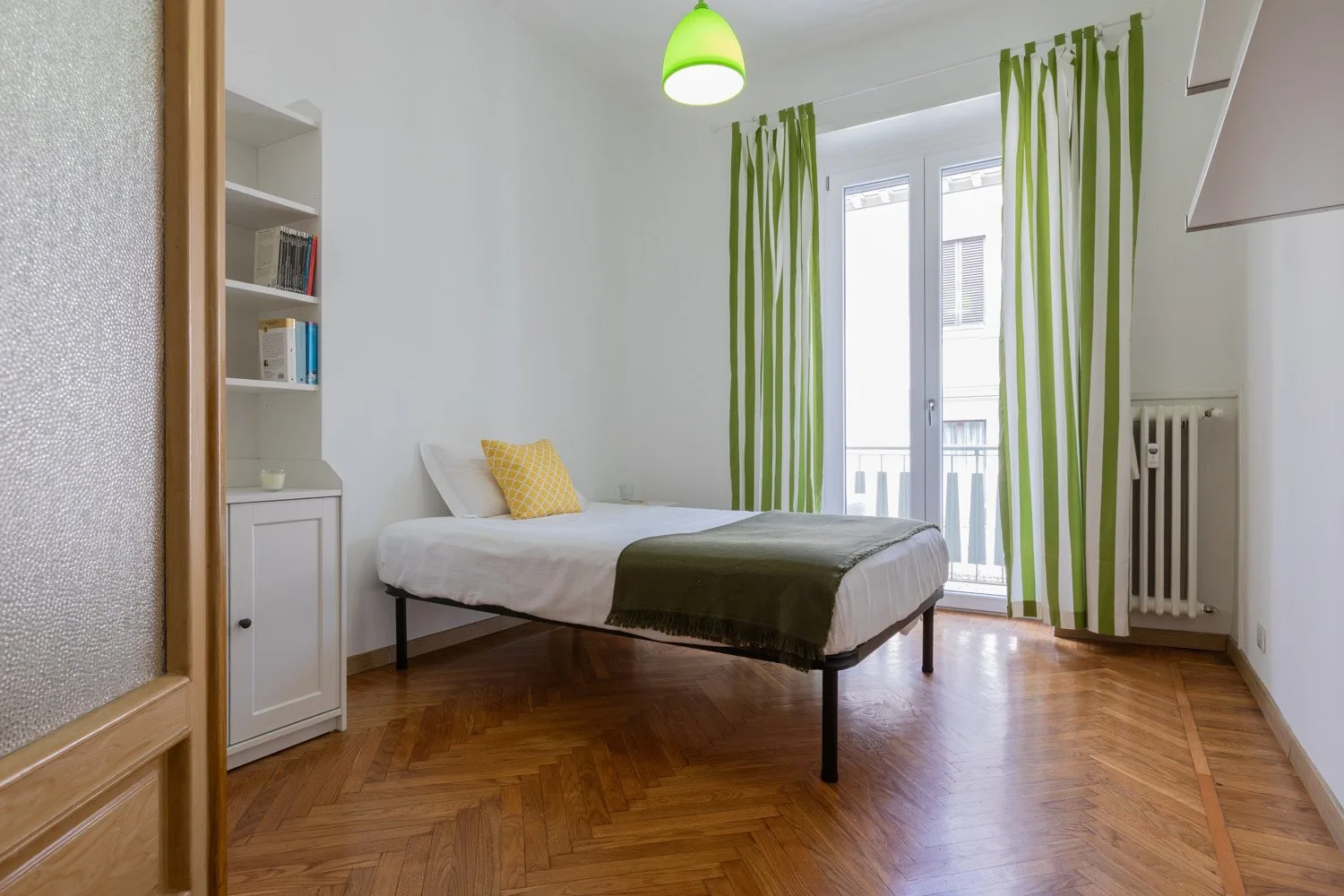 Un dormitorio luminoso con una cama, cortinas verdes y suelo de madera.