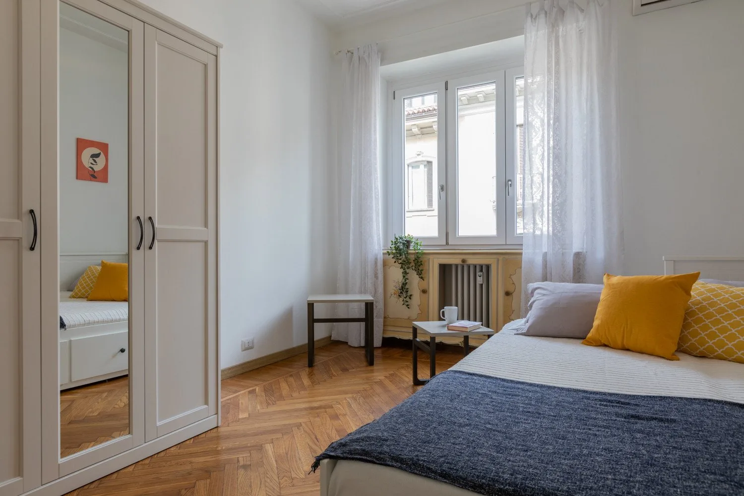Un dormitorio con una cama, un armario y una ventana enmarcada por cortinas translúcidas.