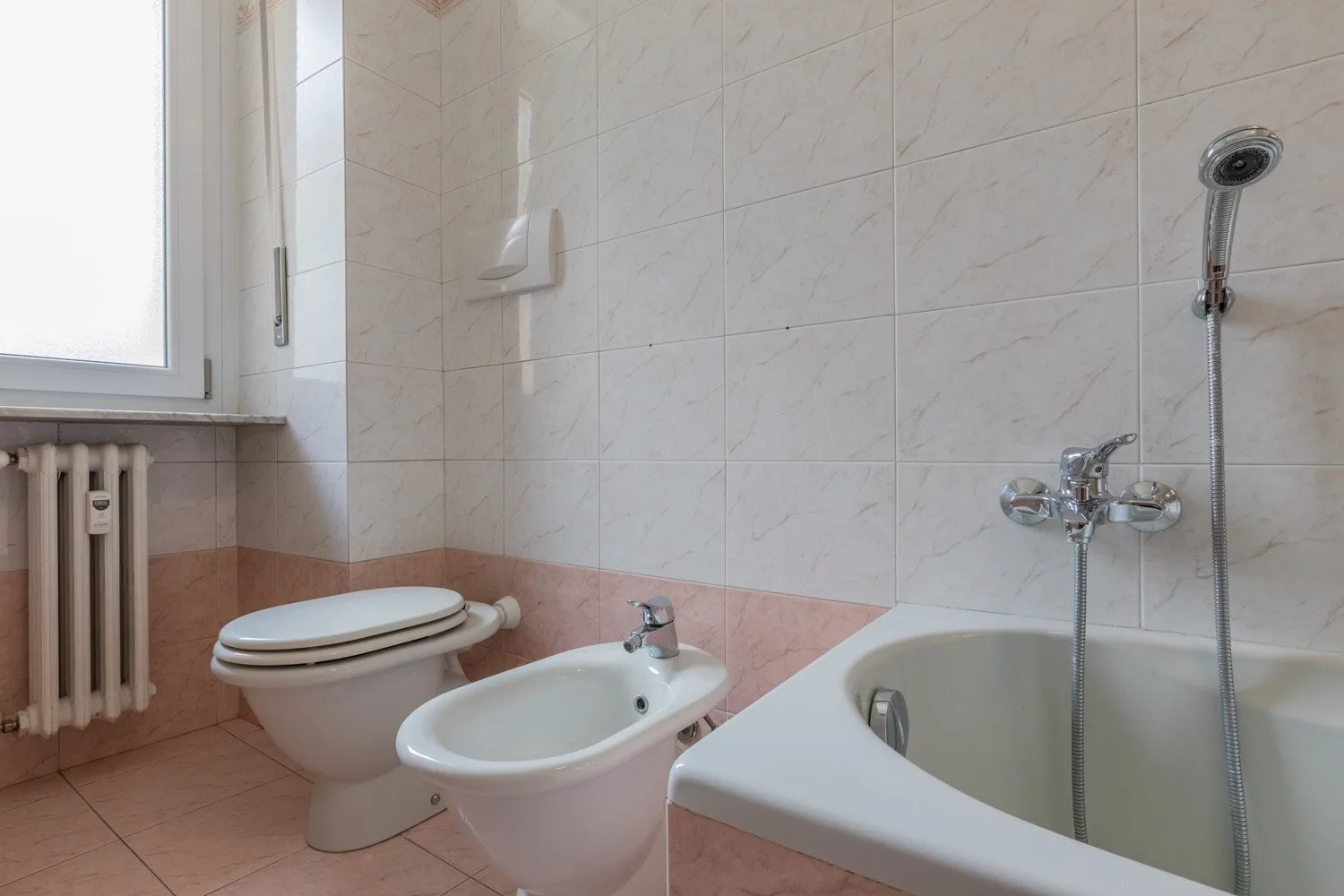 Un baño alicatado con bañera, inodoro, bidé y ventana.