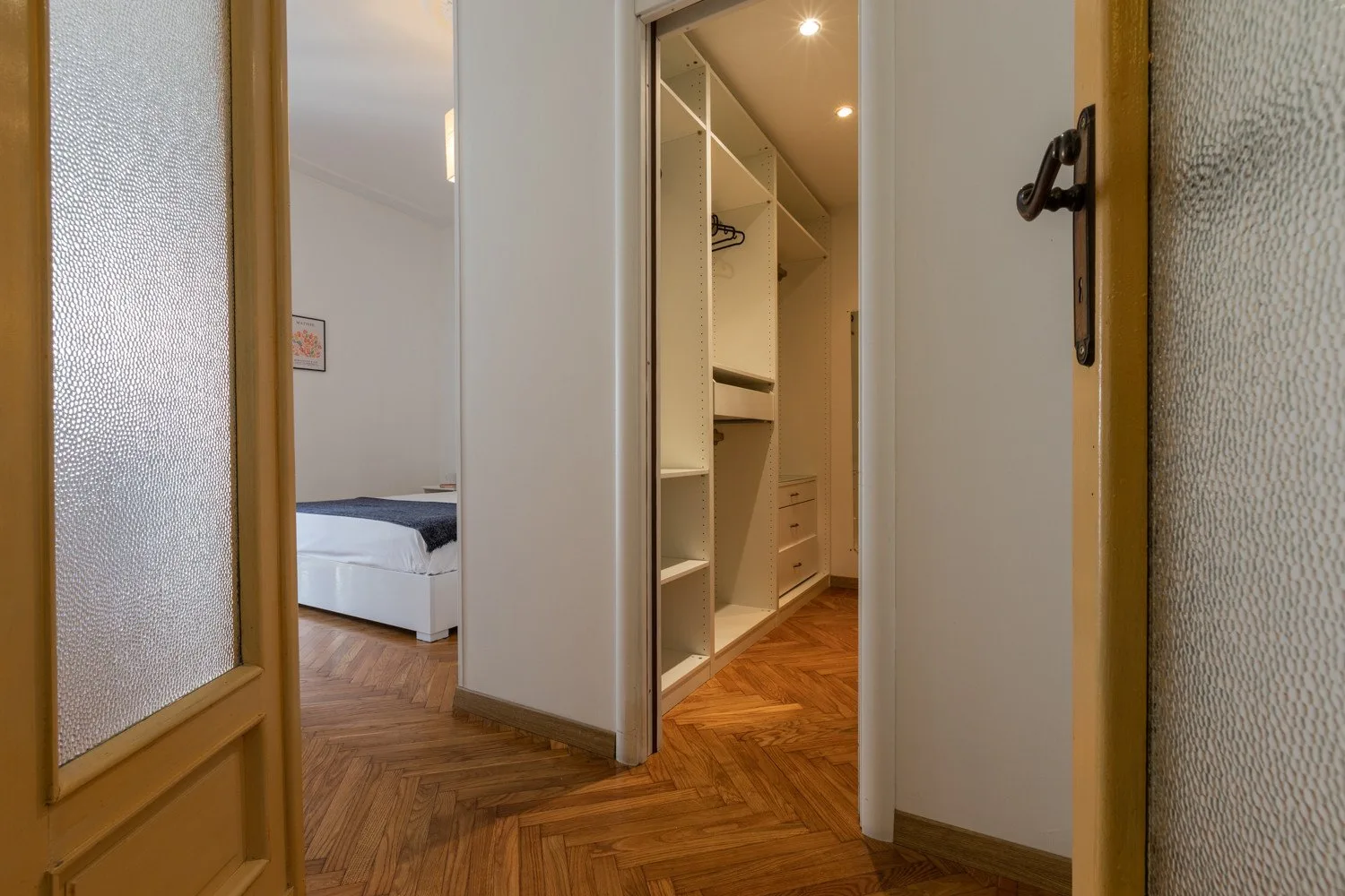 Un pasillo da a un dormitorio y a un vestidor bien iluminado.