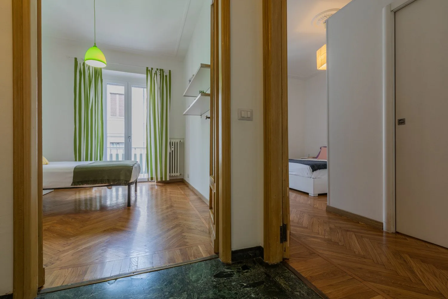 Un dormitorio con una cama, ventanas altas y cortinas verdes.