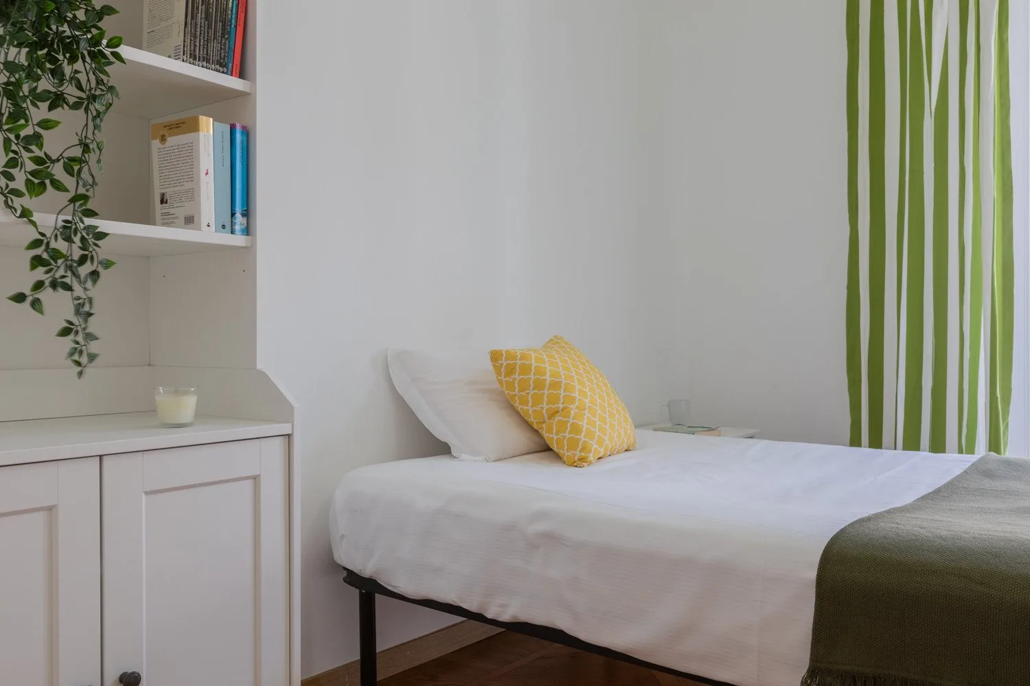 Un dormitorio con una cama blanca, una almohada amarilla y cortinas de rayas verdes.