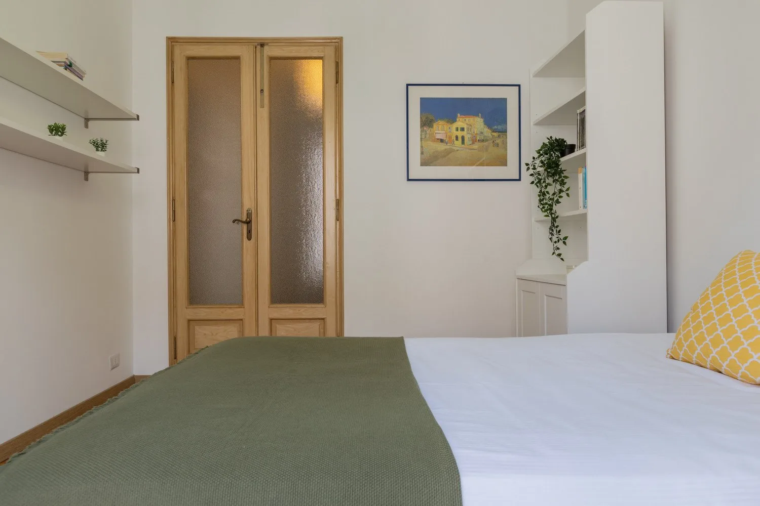 Un dormitorio con una cama, una puerta de madera y un cuadro en la pared.