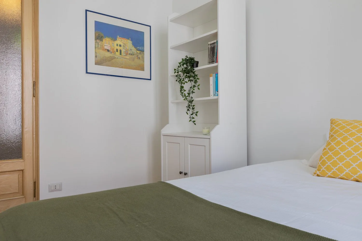 Un dormitorio con una cama, una lámina enmarcada y una estantería.