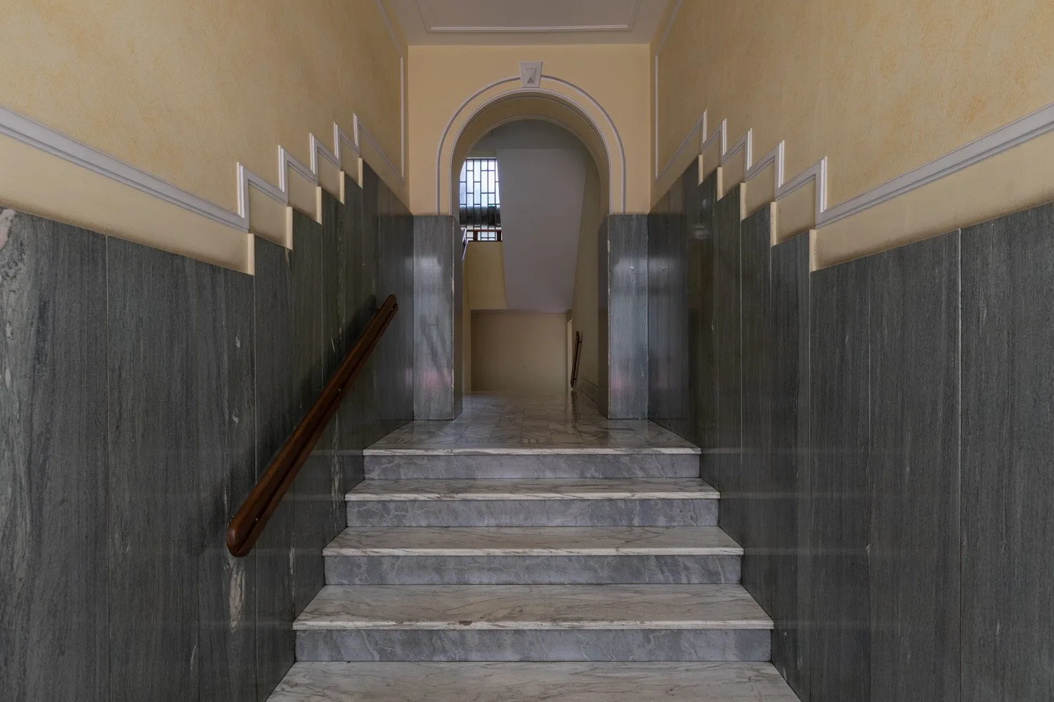 Una escalera de mármol conduce a través de un arco en un pasillo.
