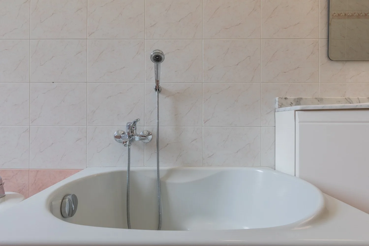 Una bañera está junto a una pared de azulejos, con una ducha de mano montada en la pared.