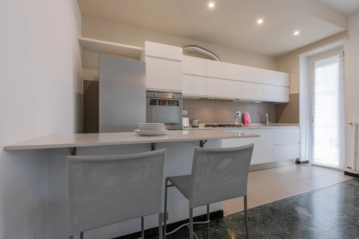Una cocina moderna con gabinetes blancos, una encimera y dos sillas.
