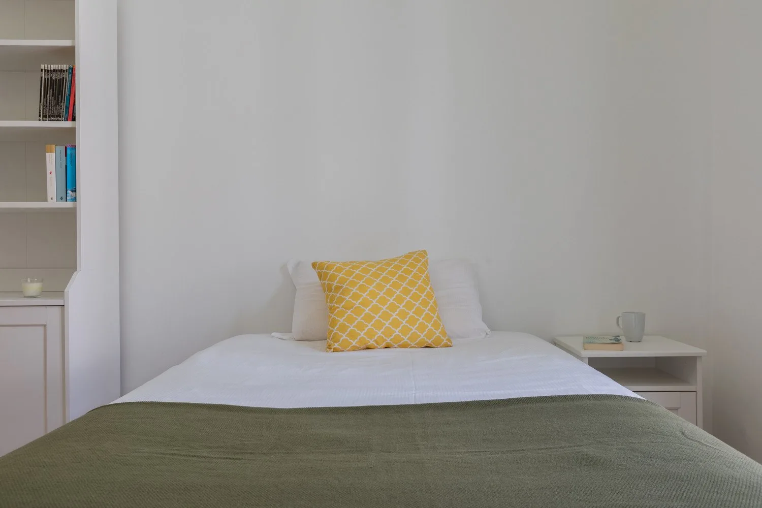 Un dormitorio con una cama tendida y un cojín amarillo estampado.
