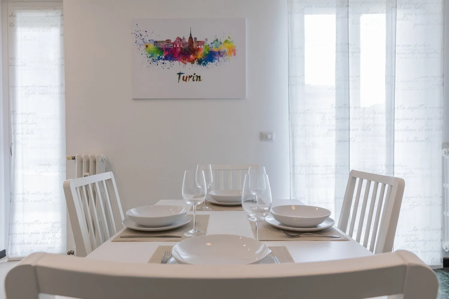 Un comedor con la mesa puesta junto a ventanas luminosas.