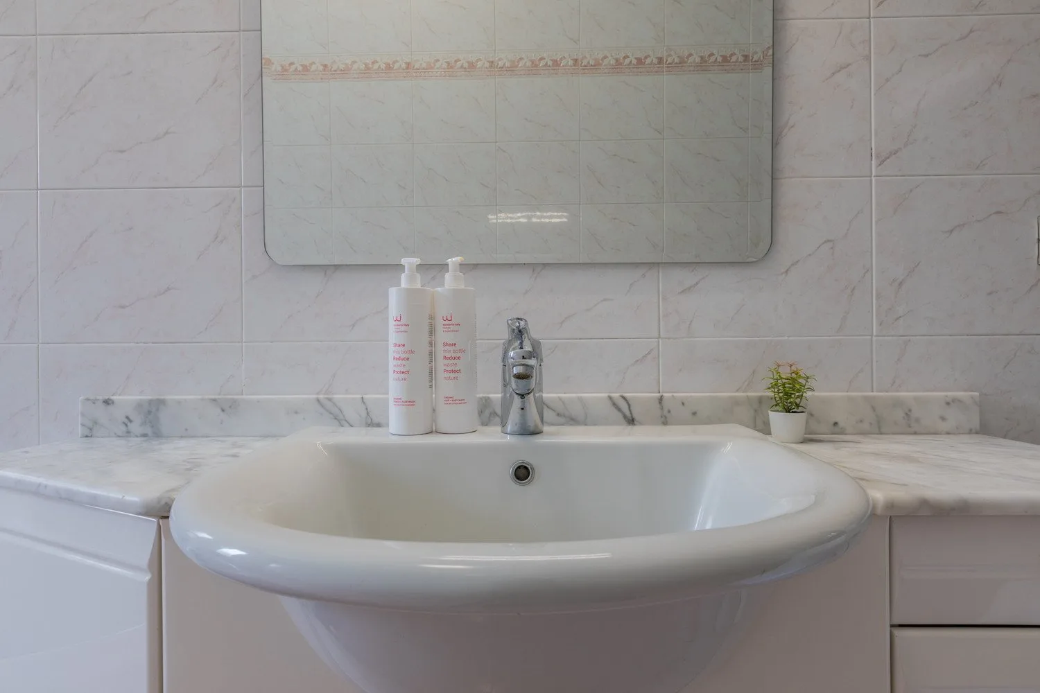 Un lavabo de baño con fregadero blanco, grifo y espejo de pared.
