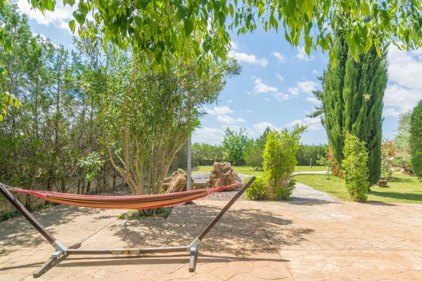 Una hamaca está sobre un patio pavimentado en un jardín con árboles frondosos.