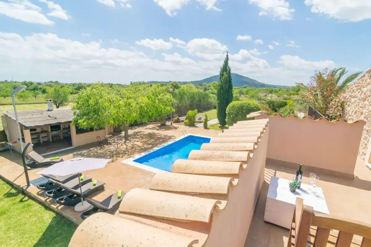 Zona de piscina exterior soleada con tumbonas, toldos curvos claros y vegetación al fondo.