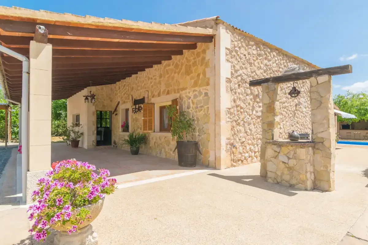 Un patio de piedra con una zona de estar sombreada y una maceta con flores en primer plano.