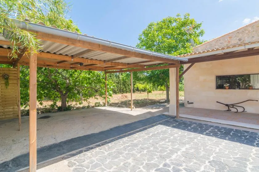 Un patio pavimentado se encuentra junto a una pérgola de madera cubierta y un edificio claro.