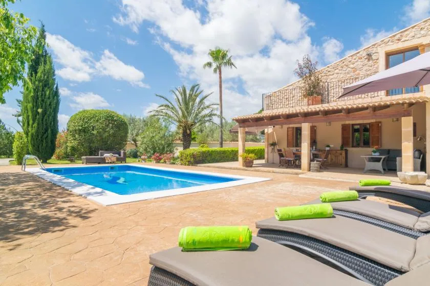 Un patio soleado junto a la piscina, con tumbonas y una zona de comedor cubierta.