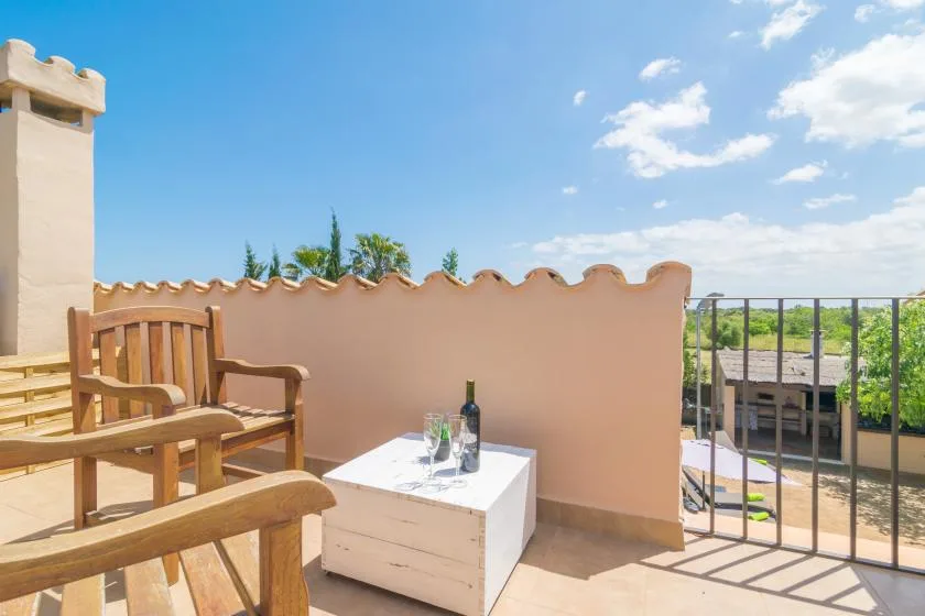 Una terraza soleada con asientos de madera y una mesa pequeña junto a una pared color durazno.