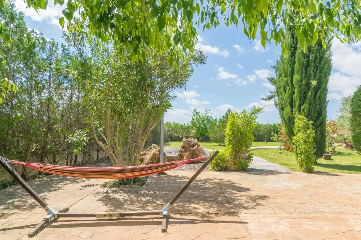 Un patio ajardinado con una hamaca bajo árboles frondosos.