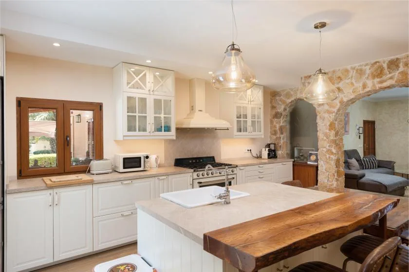 Una cocina luminosa con gabinetes blancos, una isla central y un arco de piedra.