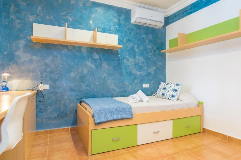 Un dormitorio colorido con una cama individual, una pared azul y estantes.