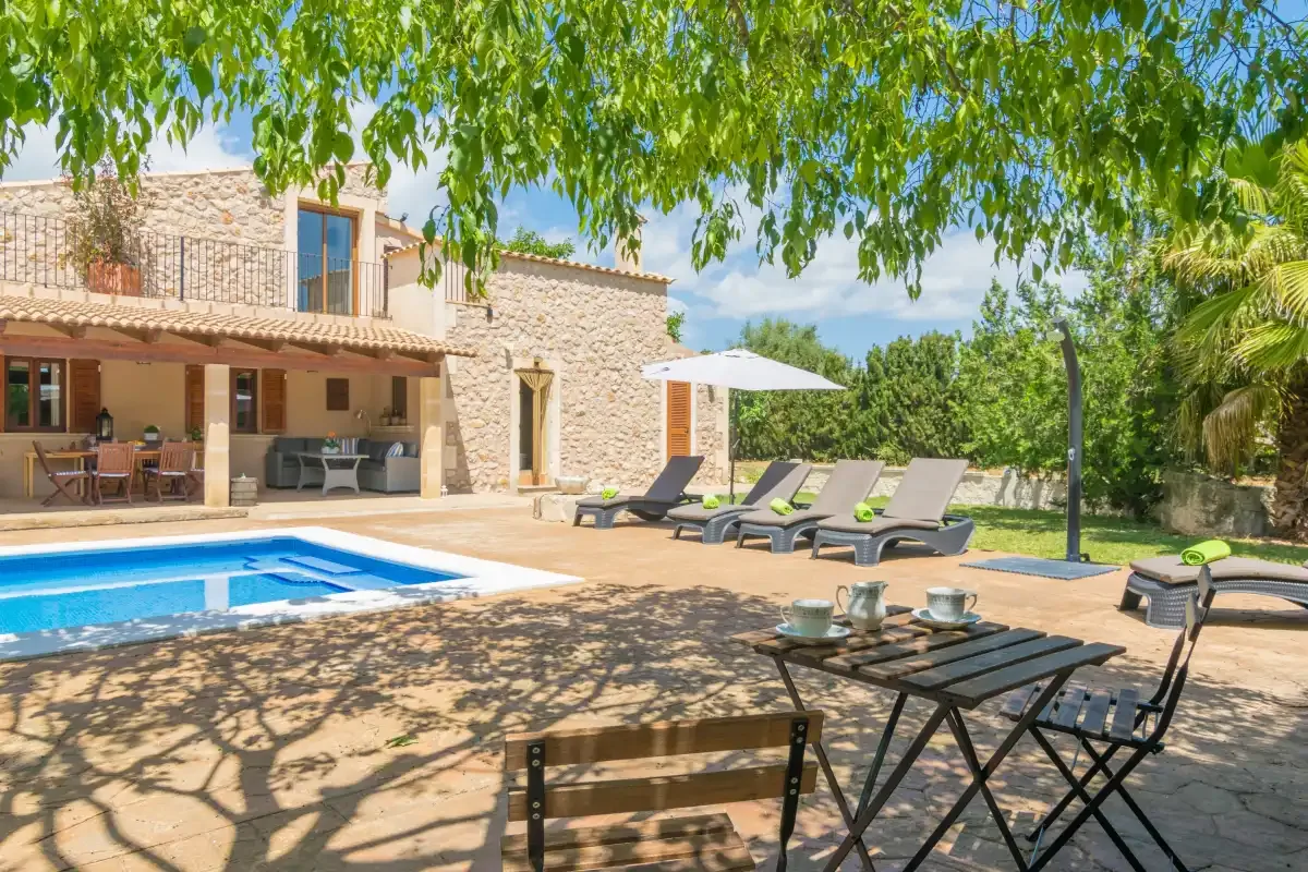Un patio soleado junto a una piscina, con asientos al aire libre y una casa de piedra.