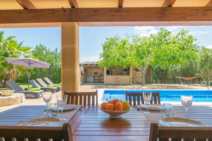 Una zona de comedor exterior cubierta da a una piscina y un jardín.