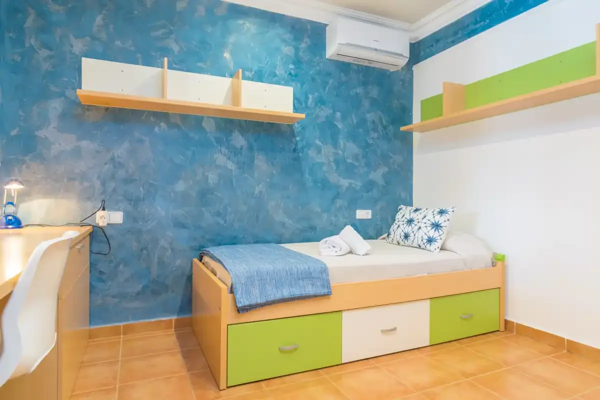 Un dormitorio con una cama individual, paredes coloridas y estantes integrados.