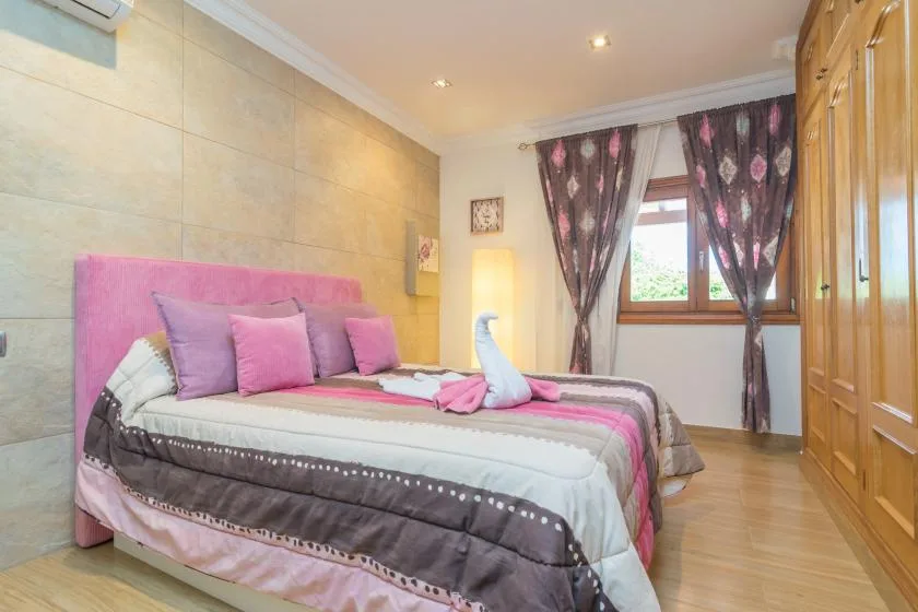 Un dormitorio con una cama, ropa de cama rosa y una ventana con cortinas oscuras.
