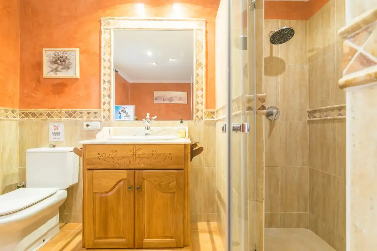Un baño con mueble de madera, inodoro y ducha con mampara de vidrio.