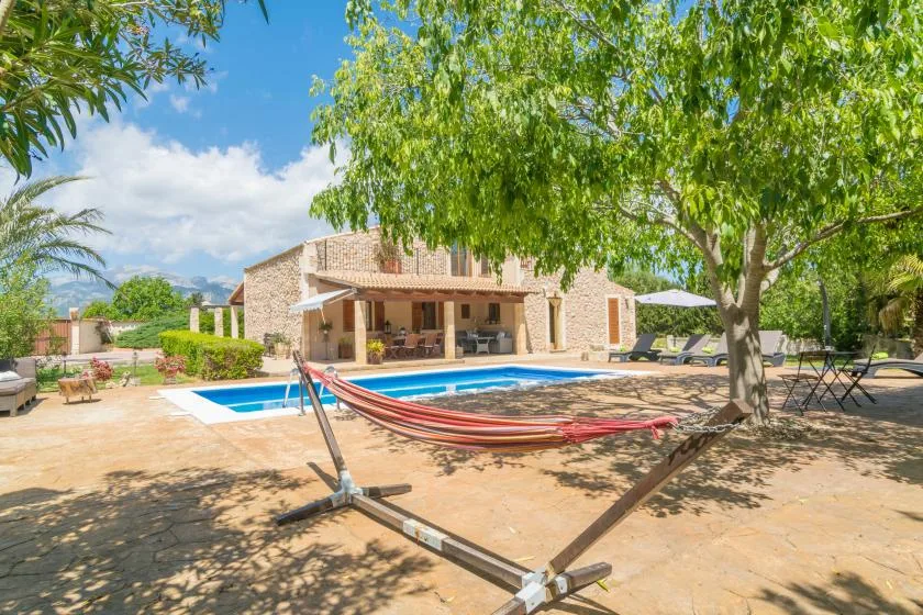 Una piscina y una hamaca están en un patio soleado junto a un edificio de piedra.